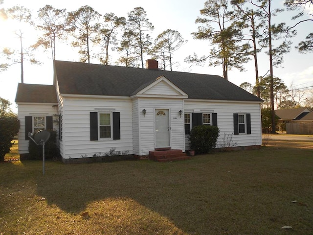 view of front facade featuring entry steps, a shingled roof, a chimney, and a front yard