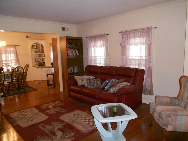 living room with ornamental molding, visible vents, built in shelves, and wood finished floors