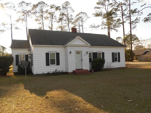 view of front facade with a shingled roof, entry steps, a chimney, and a front lawn