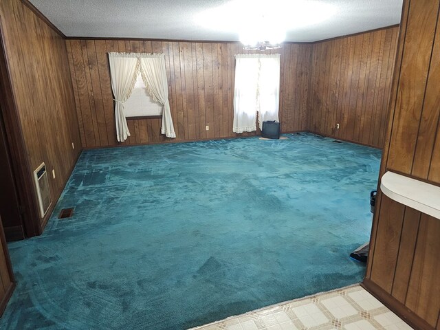 empty room with visible vents, wooden walls, a textured ceiling, and carpet flooring