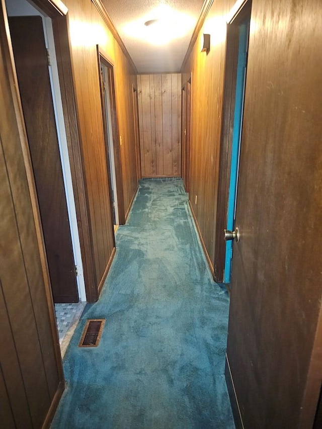 corridor featuring visible vents, wood walls, carpet, ornamental molding, and a textured ceiling