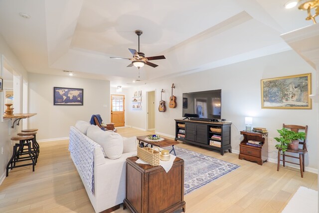 living room with a tray ceiling, baseboards, light wood finished floors, and ceiling fan