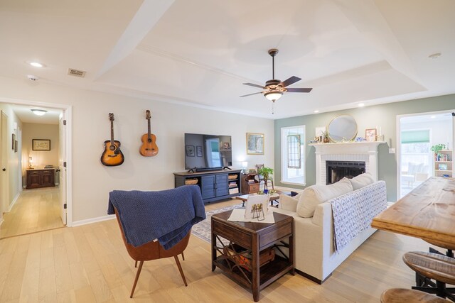 living room featuring visible vents, ceiling fan, light wood-style floors, a raised ceiling, and a brick fireplace
