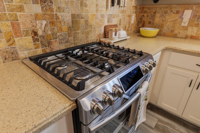 room details featuring white cabinetry, light stone counters, gas stove, and backsplash