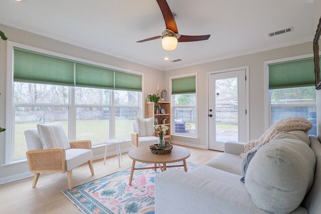 living area with a ceiling fan, visible vents, light wood finished floors, and ornamental molding