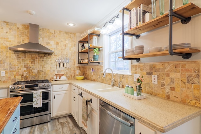 kitchen with open shelves, a sink, stainless steel appliances, wall chimney range hood, and butcher block counters
