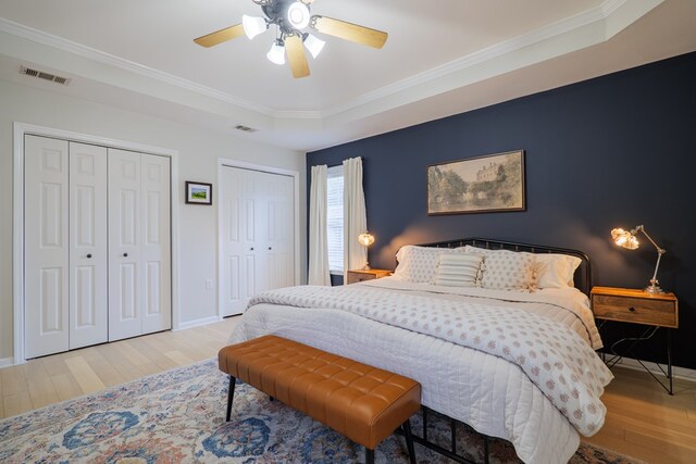 bedroom with wood finished floors, visible vents, two closets, and ornamental molding