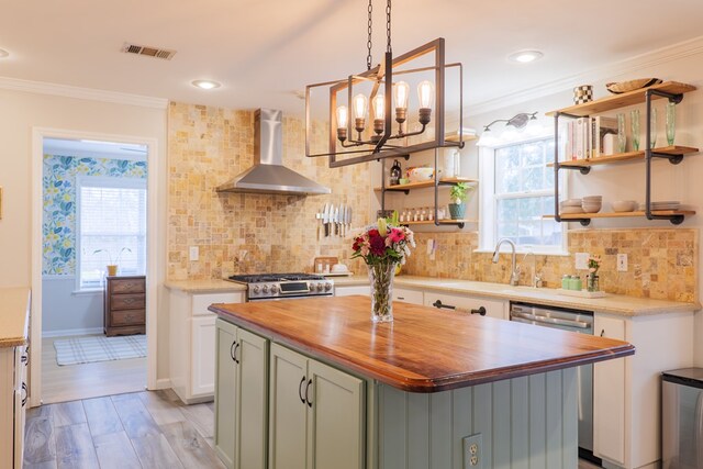 kitchen featuring stove, wooden counters, crown molding, and wall chimney range hood