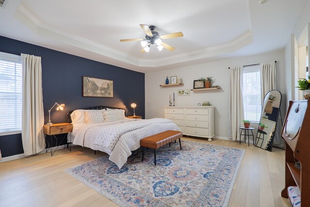bedroom with a raised ceiling, light wood-style flooring, ornamental molding, and ceiling fan