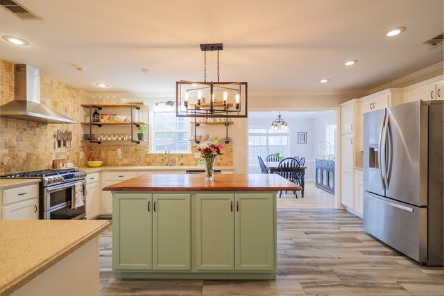 kitchen featuring a notable chandelier, wood counters, appliances with stainless steel finishes, wall chimney range hood, and green cabinetry