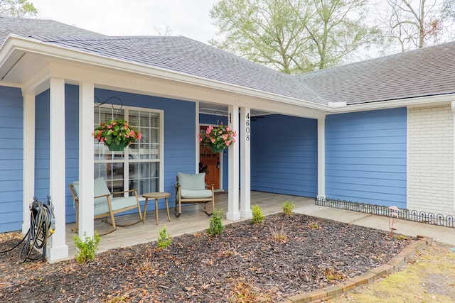 property entrance with brick siding, covered porch, and roof with shingles