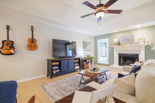 living room with a raised ceiling, light wood-style floors, baseboards, a brick fireplace, and ceiling fan
