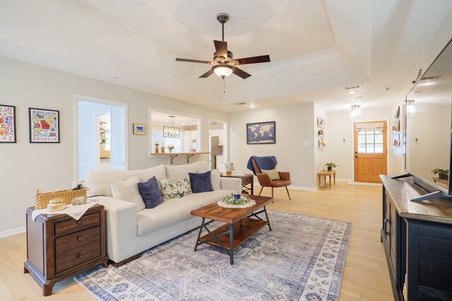 living room featuring ceiling fan, baseboards, a raised ceiling, and light wood-style flooring