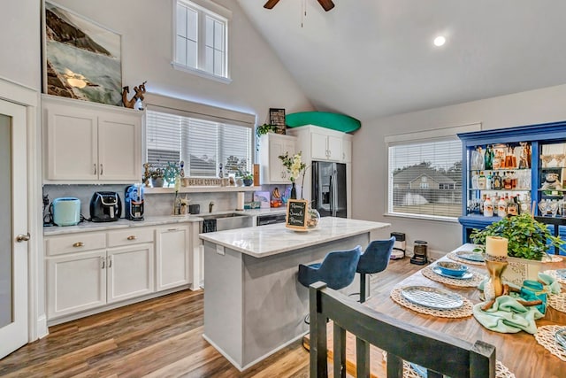 kitchen with a ceiling fan, white cabinetry, black fridge, light wood-type flooring, and a center island