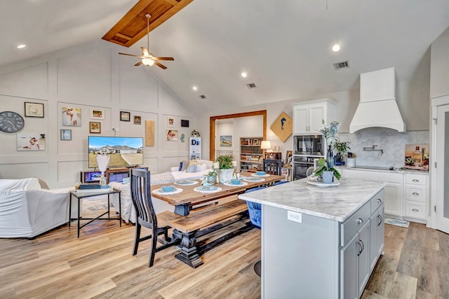 kitchen featuring a center island, stainless steel appliances, custom range hood, a decorative wall, and visible vents