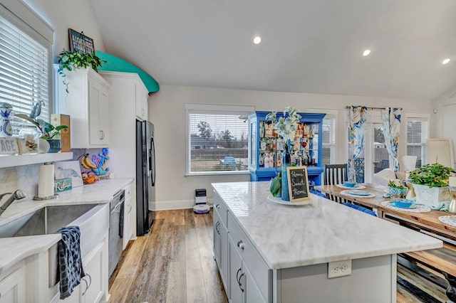 kitchen with freestanding refrigerator, white cabinetry, vaulted ceiling, a kitchen island, and dishwasher