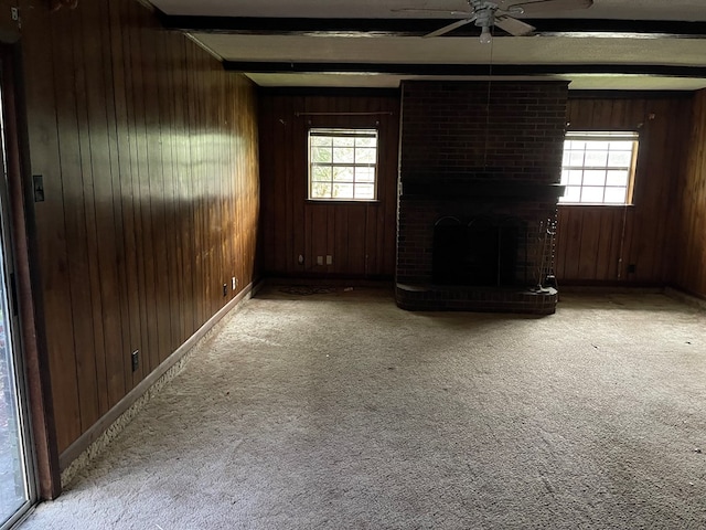 unfurnished living room with beam ceiling, a fireplace, wood walls, and plenty of natural light