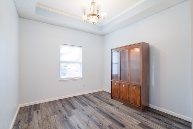 empty room with crown molding, dark hardwood / wood-style floors, a raised ceiling, and a notable chandelier