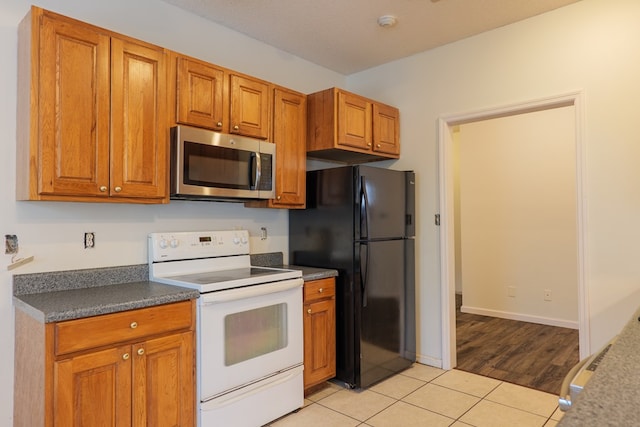 kitchen with light tile patterned flooring, black fridge, a textured ceiling, and white range with electric cooktop