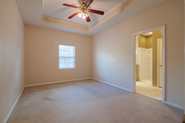 unfurnished room with a raised ceiling, ornamental molding, light colored carpet, and ceiling fan