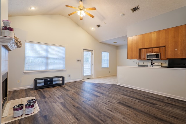 living room featuring hardwood / wood-style flooring, ceiling fan, high vaulted ceiling, a textured ceiling, and a tiled fireplace