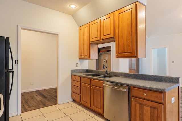 kitchen with light tile patterned flooring, dishwasher, lofted ceiling, sink, and black fridge