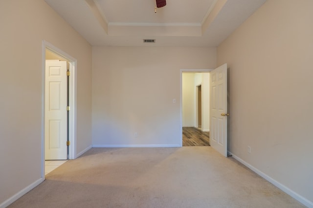 unfurnished room featuring a raised ceiling, ornamental molding, light carpet, and ceiling fan