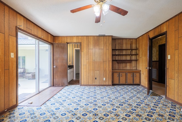 unfurnished bedroom featuring baseboards, wooden walls, a textured ceiling, and access to exterior