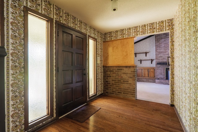 foyer entrance featuring dark wood-style flooring, wallpapered walls, and a textured ceiling