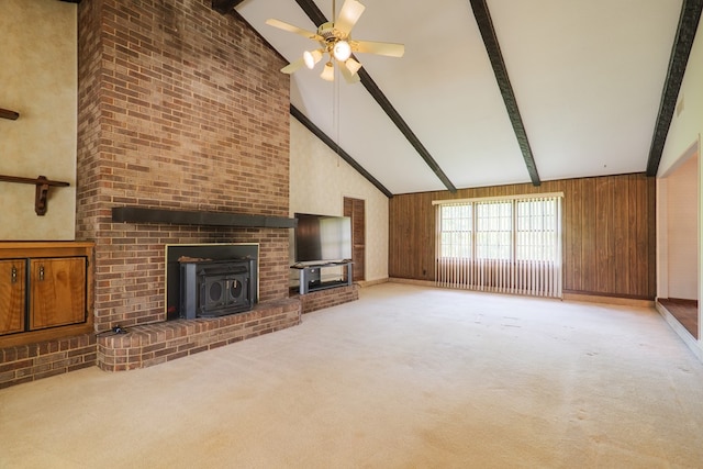 unfurnished living room with a wood stove, high vaulted ceiling, carpet floors, beamed ceiling, and a ceiling fan