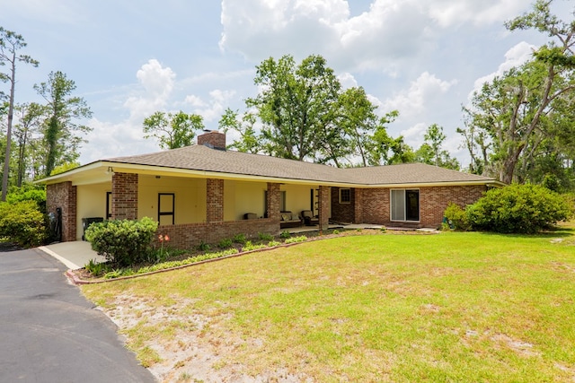 ranch-style house featuring a chimney, a front yard, brick siding, and aphalt driveway