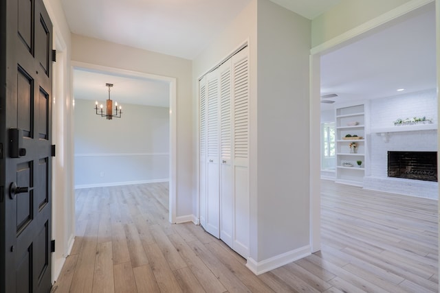 corridor featuring an inviting chandelier, light wood-style flooring, baseboards, and built in shelves