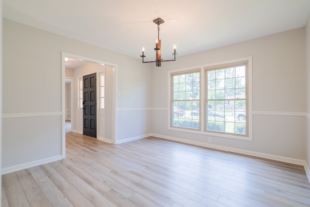 spare room featuring baseboards, an inviting chandelier, and light wood-style flooring