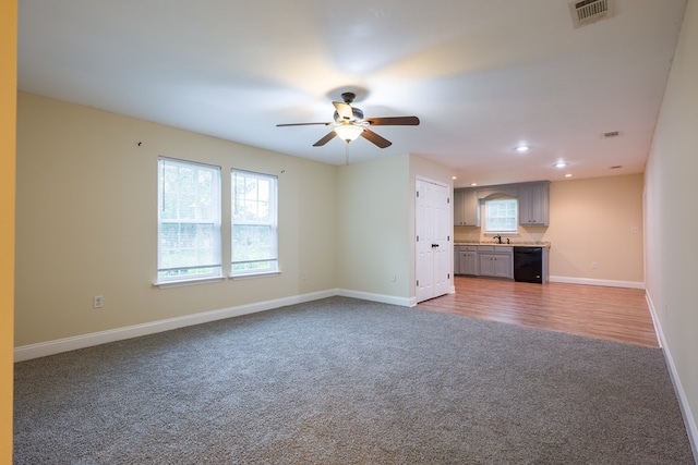 unfurnished living room featuring a wealth of natural light, sink, ceiling fan, and wood-type flooring