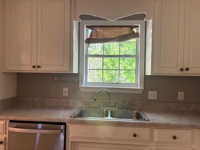 kitchen with stainless steel dishwasher, white cabinets, light countertops, and a sink