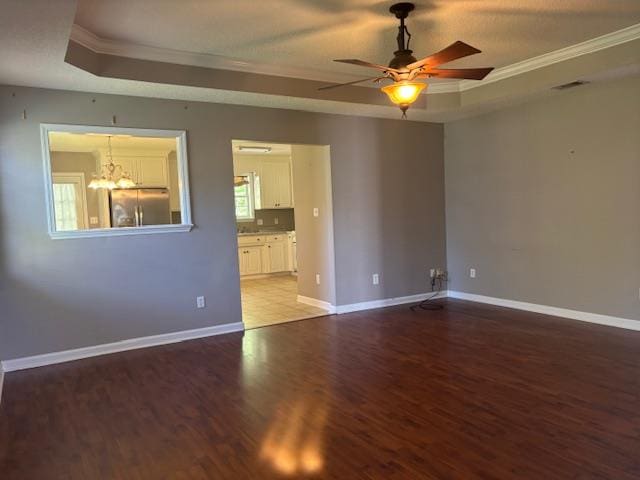 unfurnished room with a tray ceiling, baseboards, wood finished floors, and ceiling fan with notable chandelier