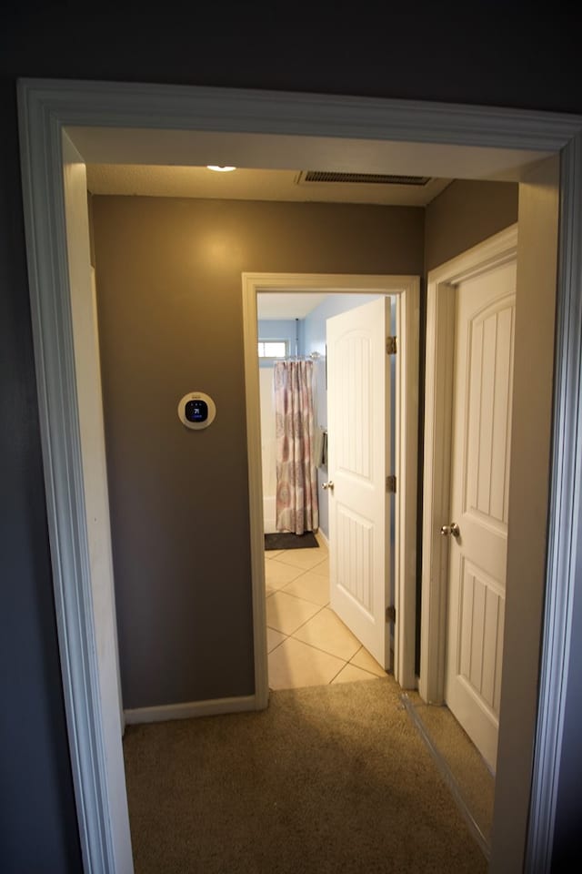 hallway with light colored carpet, visible vents, baseboards, and light tile patterned flooring