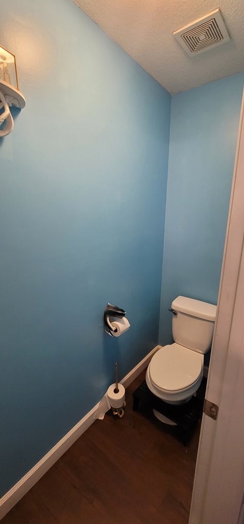 bathroom with visible vents, toilet, a textured ceiling, wood finished floors, and baseboards