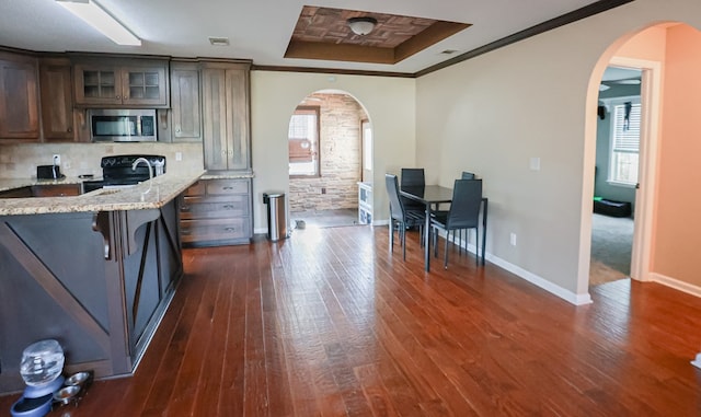 kitchen with a tray ceiling, arched walkways, black electric range oven, and stainless steel microwave