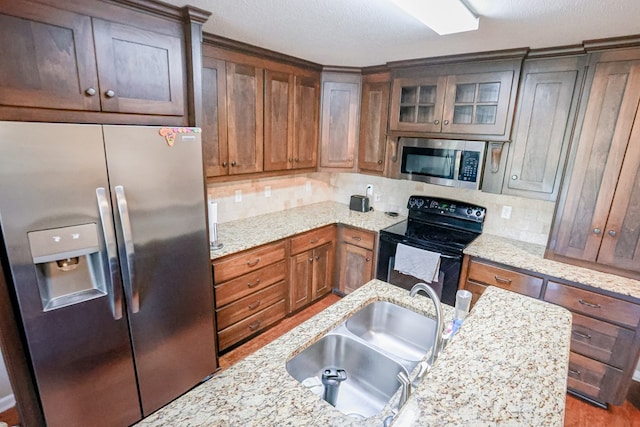 kitchen featuring a sink, tasteful backsplash, light stone countertops, appliances with stainless steel finishes, and glass insert cabinets