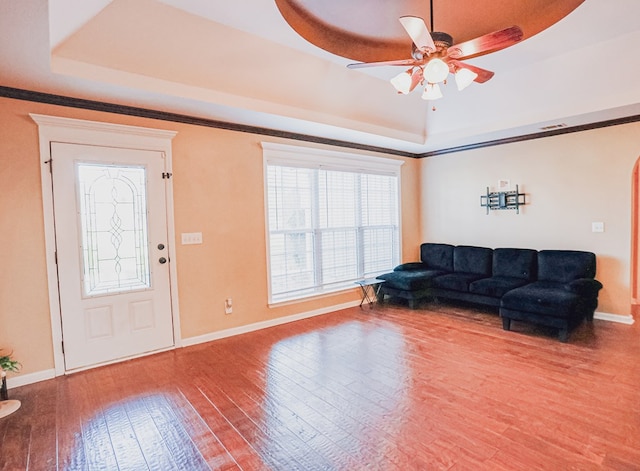 living area featuring hardwood / wood-style flooring, baseboards, a ceiling fan, and a raised ceiling