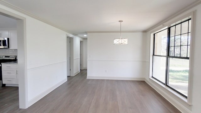 unfurnished dining area featuring crown molding, baseboards, and wood finished floors