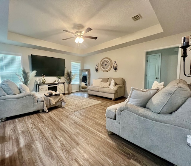 living area with a ceiling fan, wood finished floors, visible vents, and a raised ceiling