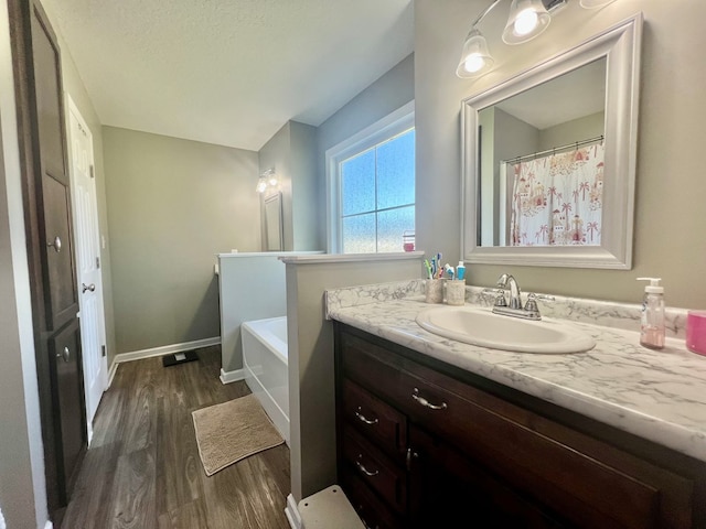 full bath with wood finished floors, vanity, baseboards, and a bathtub