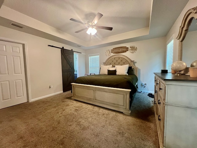carpeted bedroom with a barn door, ceiling fan, a raised ceiling, baseboards, and visible vents