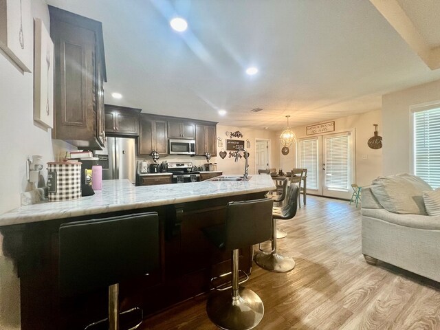 kitchen with stainless steel appliances, a peninsula, light wood-style floors, and light stone counters