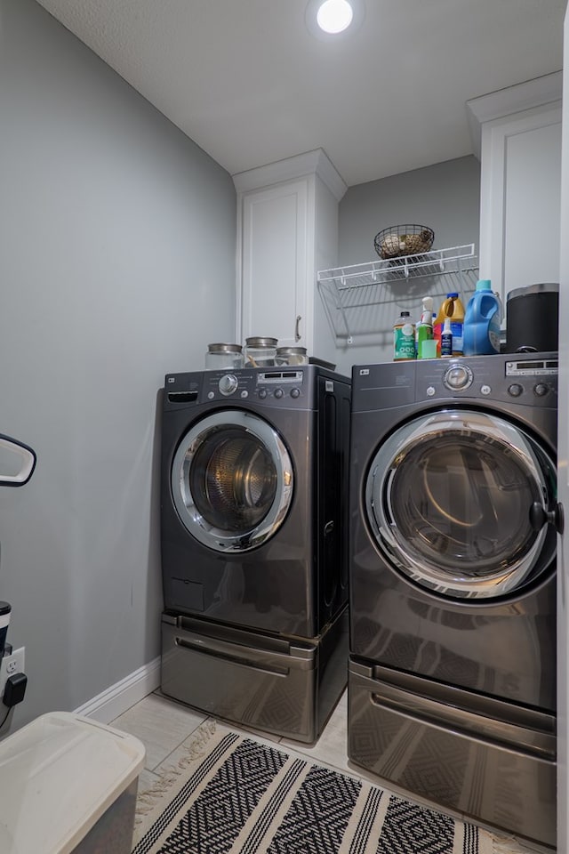 clothes washing area with cabinet space, washer and dryer, and baseboards