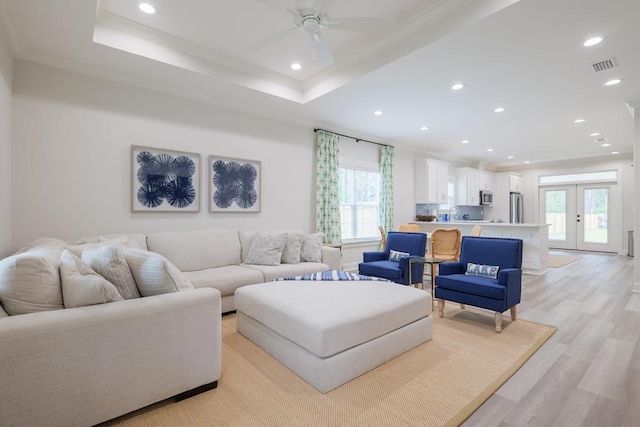 living room with french doors, light hardwood / wood-style flooring, ornamental molding, a raised ceiling, and ceiling fan