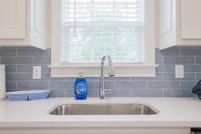 interior details with tasteful backsplash, sink, white cabinets, and light stone counters