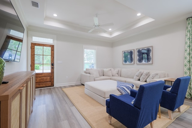 living room featuring a raised ceiling, ornamental molding, and a healthy amount of sunlight